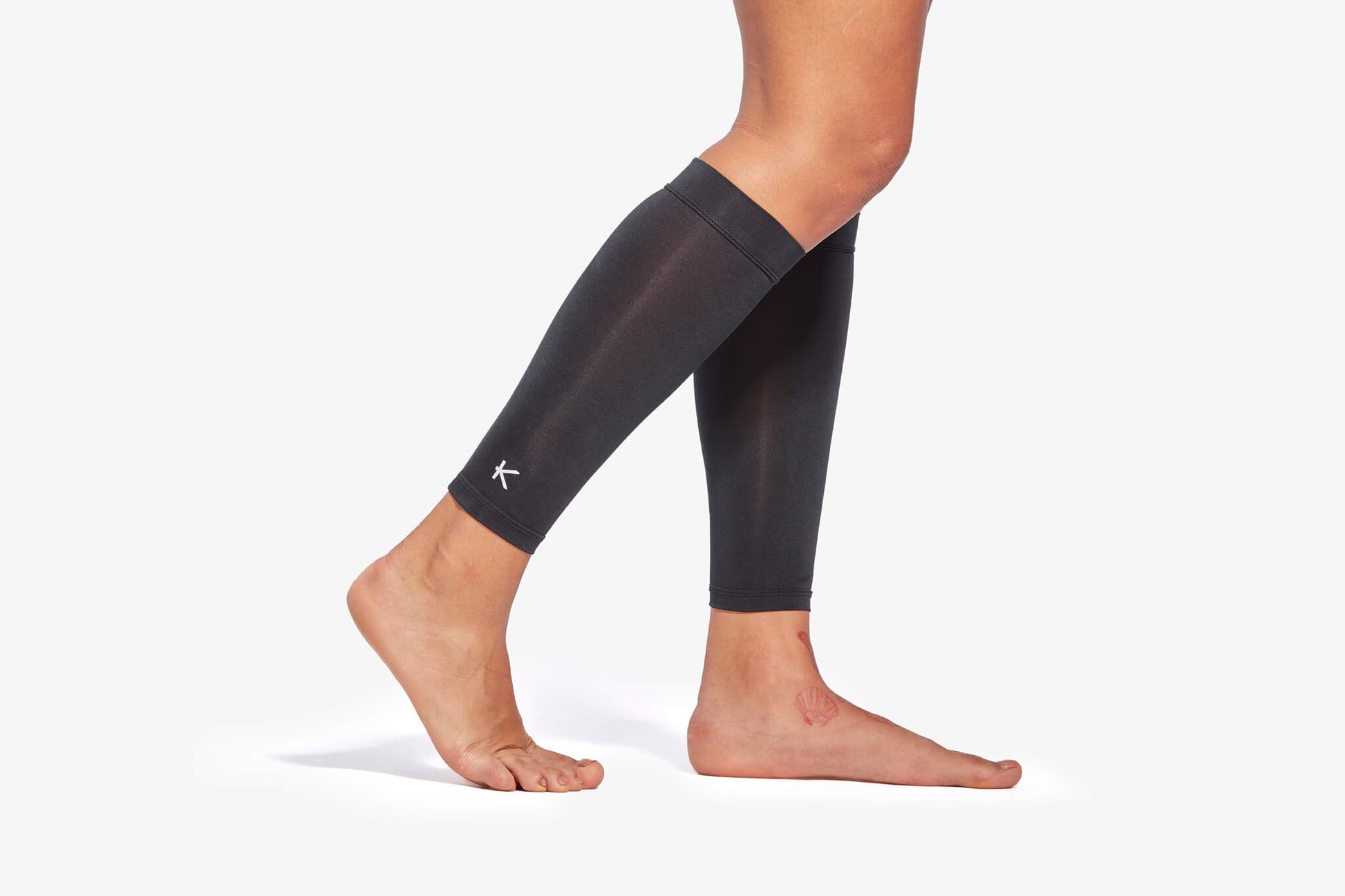 Person wearing black compression leg sleeves on a white background