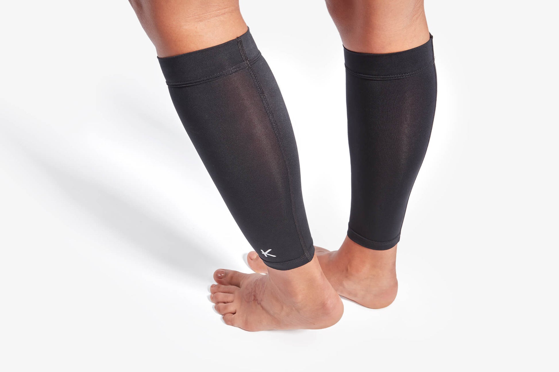 Black compression leg sleeves on a person's legs against a white background