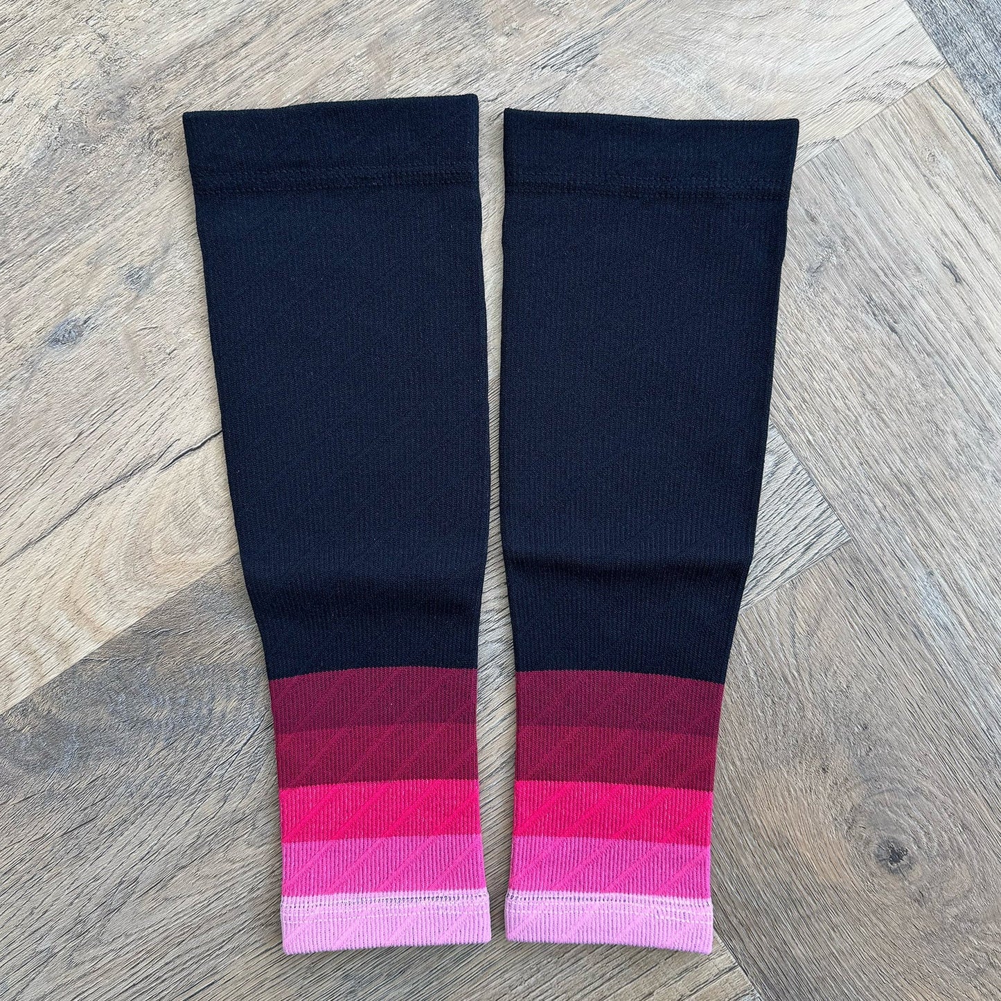 Pair of black knee-high socks with pink and red striped cuffs on a wooden floor.
