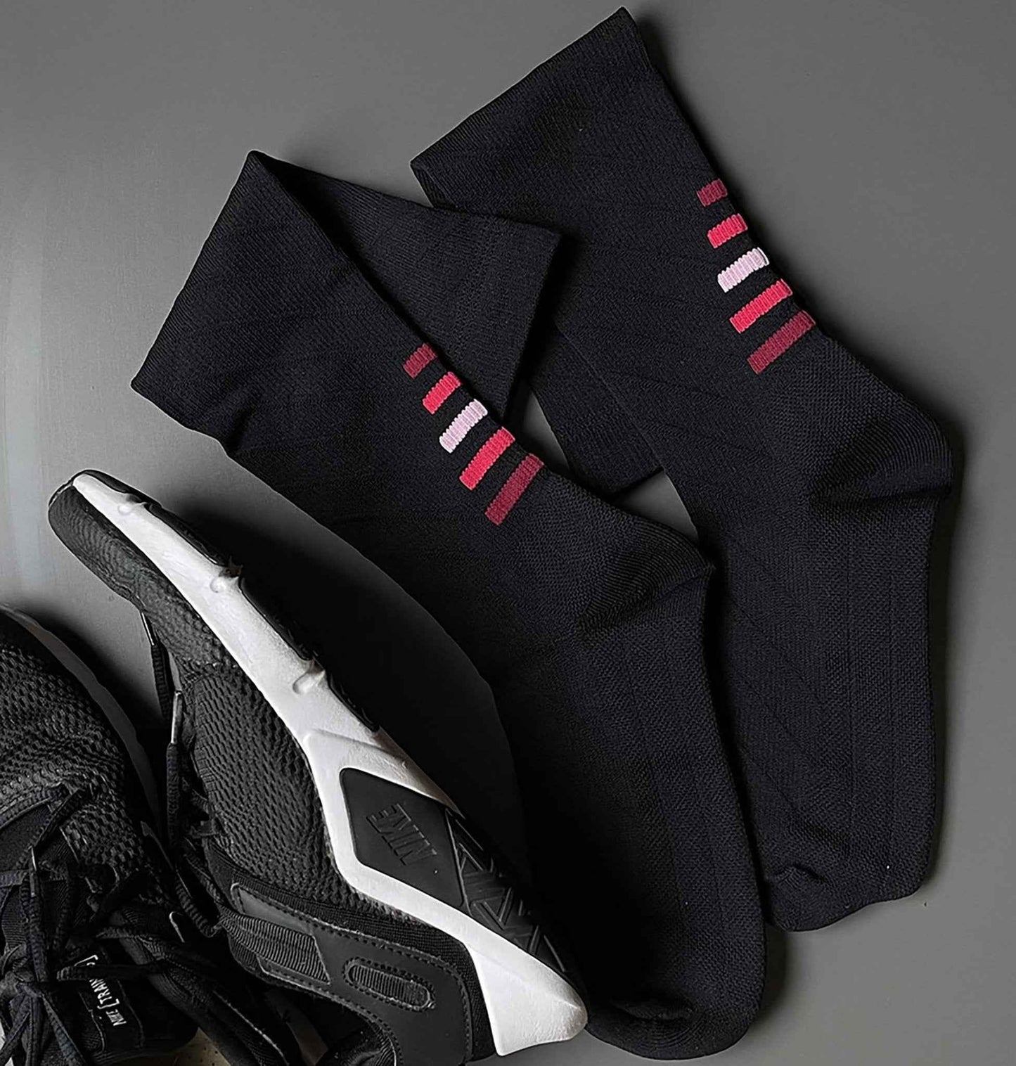 Black socks with red and white stripes on a gray surface with a sneaker.