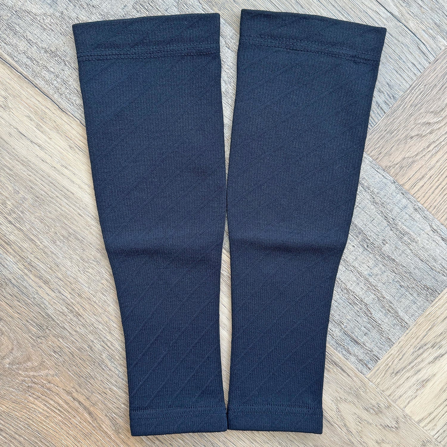 Pair of navy blue compression sleeves on a wooden floor.