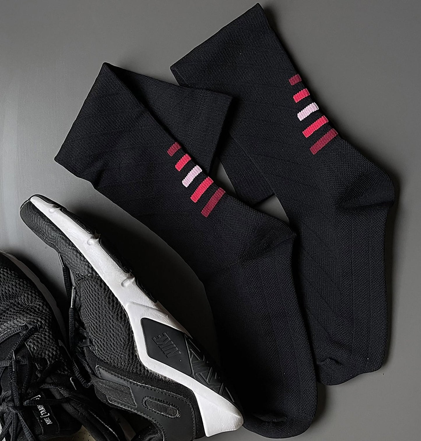 Black socks with red and white stripes on a gray surface with a sneaker.